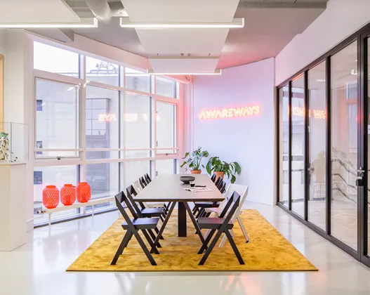 Foto van de entree van het kantoor van Awareways in Utrecht, met een tafel en stoelen en een neonversie van het logo aan de muur.