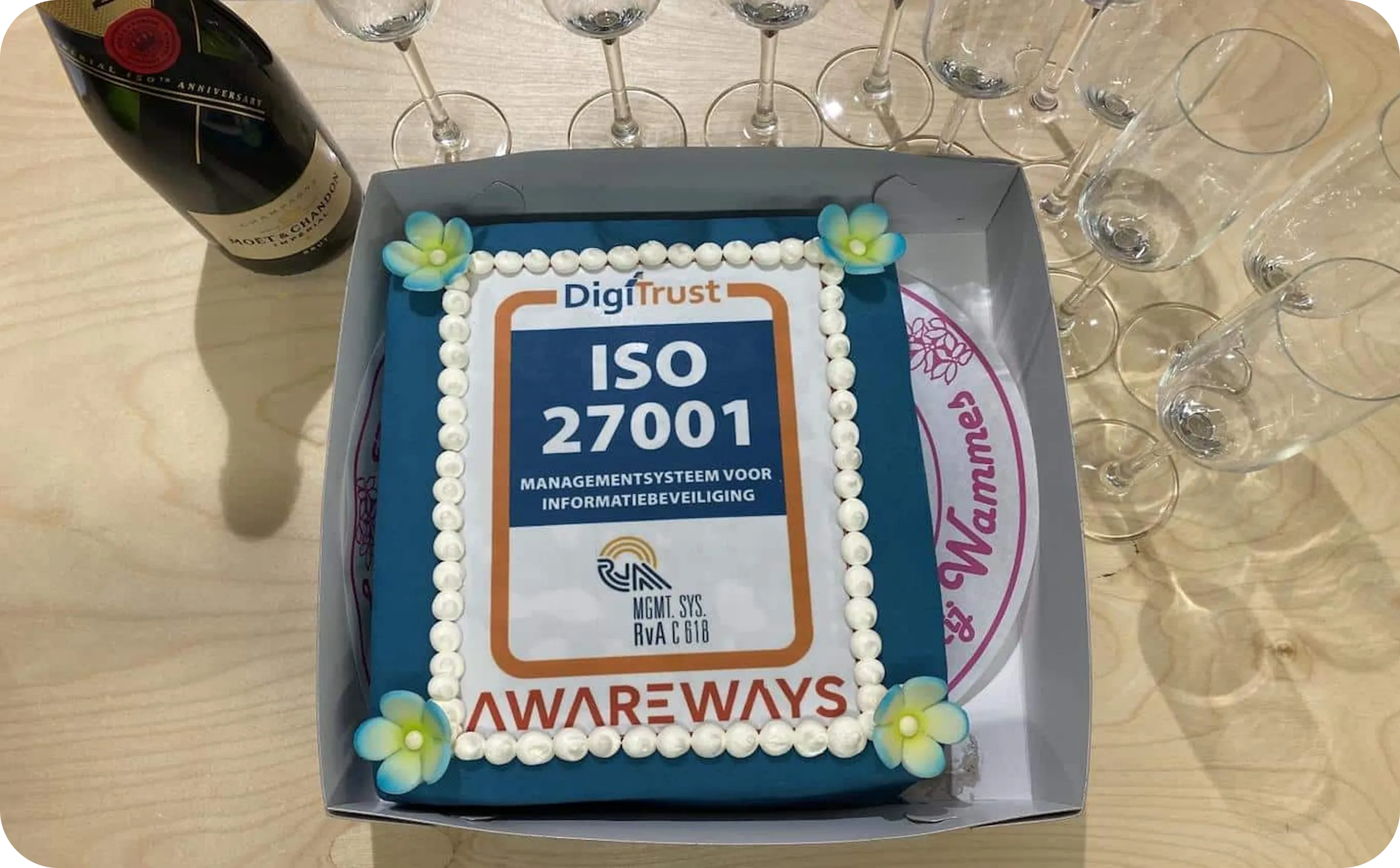 Een taart met het ISO 9001-logo (certificaat voor kwaliteitsmanagementsysteem), enkele glazen en een fles champagne.