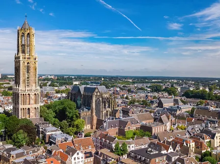 Aerial view of the city of Utrecht, Netherlands, featuring the tall Gothic Dom Tower standing next to the Dom Cathedral, surrounded by historic city buildings.