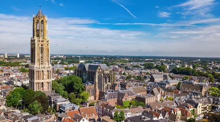Aerial view of the city of Utrecht, Netherlands, featuring the tall Gothic Dom Tower standing next to the Dom Cathedral, surrounded by historic city buildings.